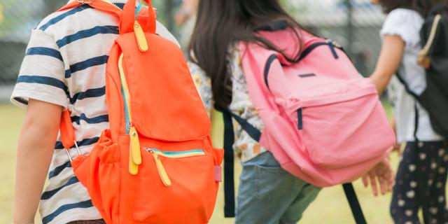 Three pupils of primary school go hand in hand. Boy and girl with school bags behind the back. Beginning of school lessons. Warm day of fall. Back to school. Little first graders.